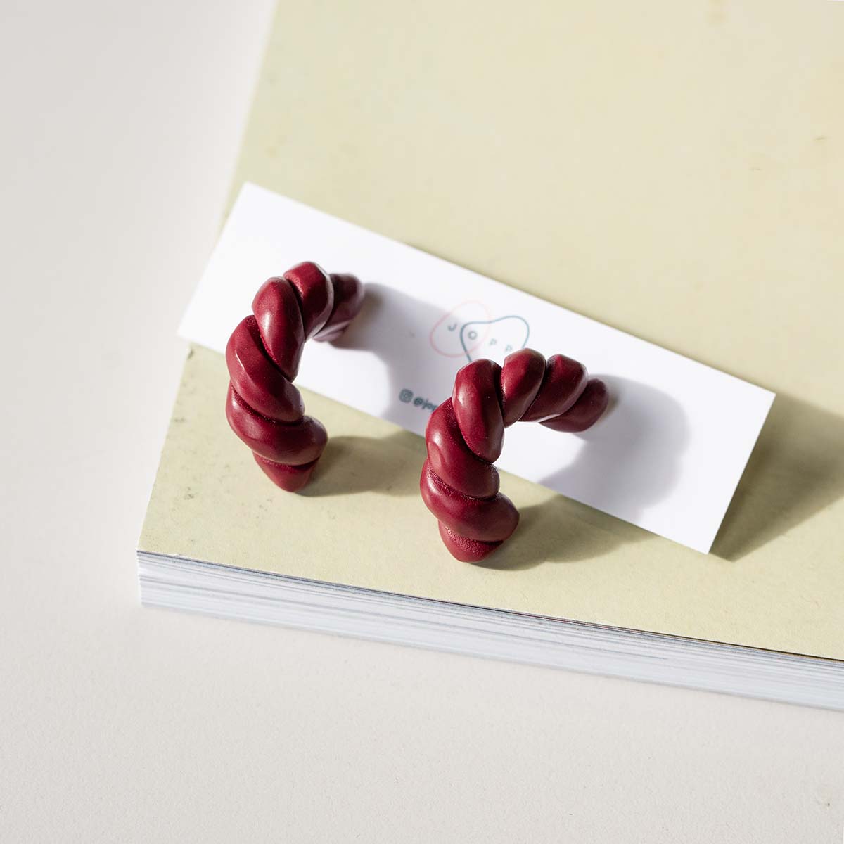 Maroon twisted polymer clay earrings photographed on a book