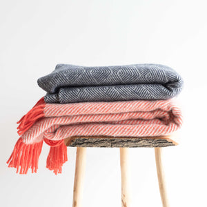 A grey blanket and a red blanket with frills folded on too of a stool - white background