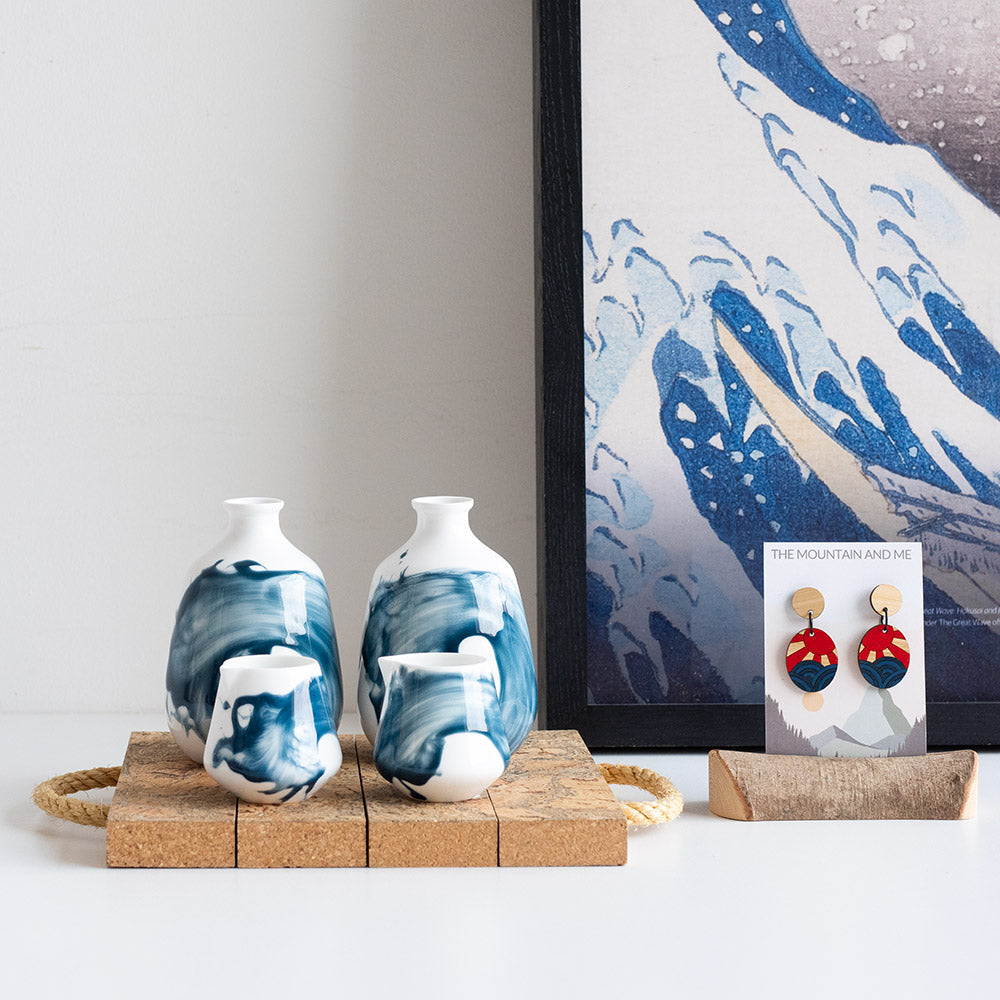 Some ceramic products on a cork surface, with some earrings to the side placed in front of an art poster.