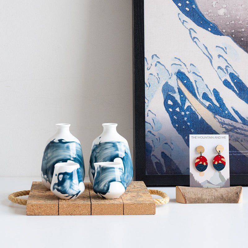 Some ceramic products on a cork surface, with some earrings to the side placed in front of an art poster.
