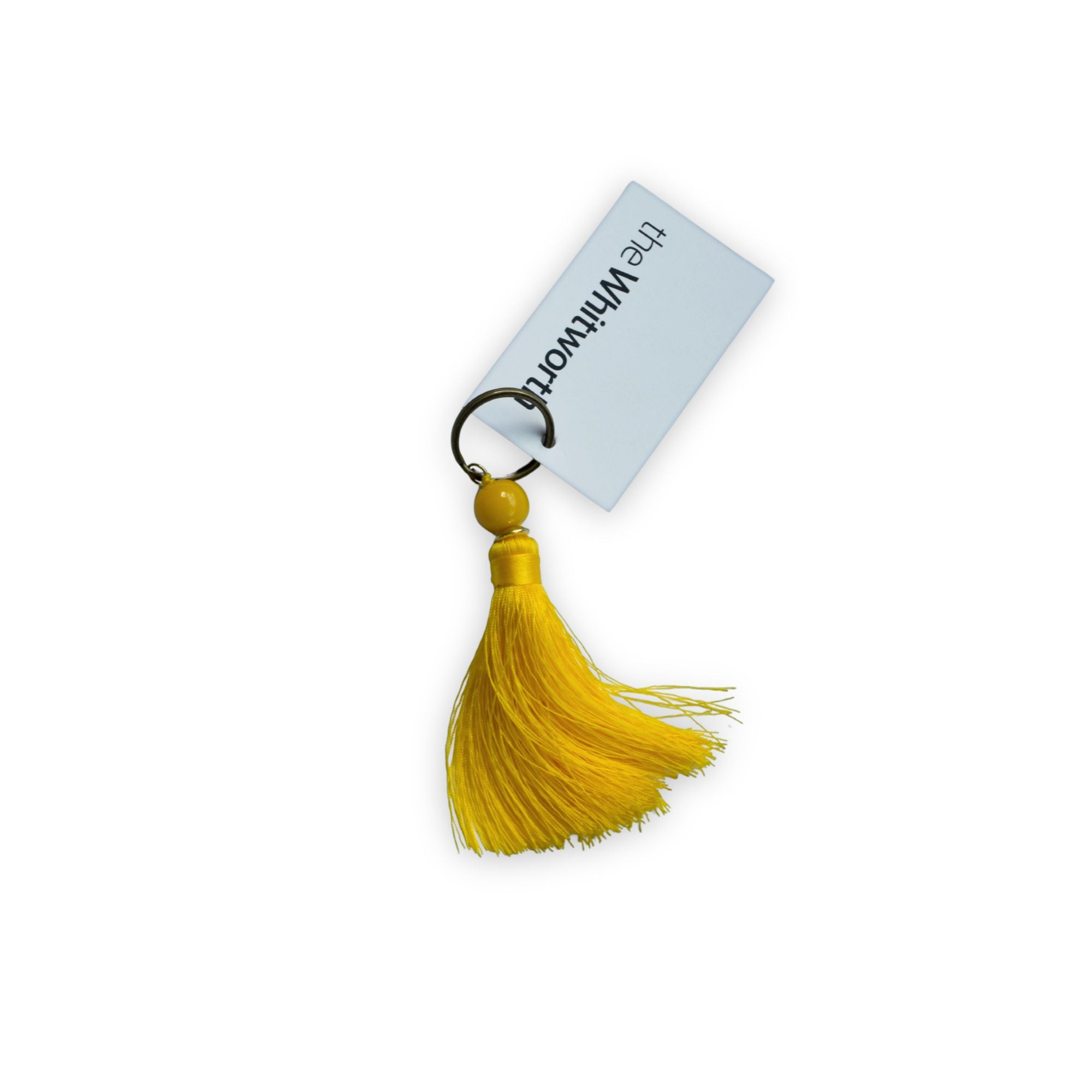 A yellow tassel keychain with a swing tag printed with 'the Whitworth'.