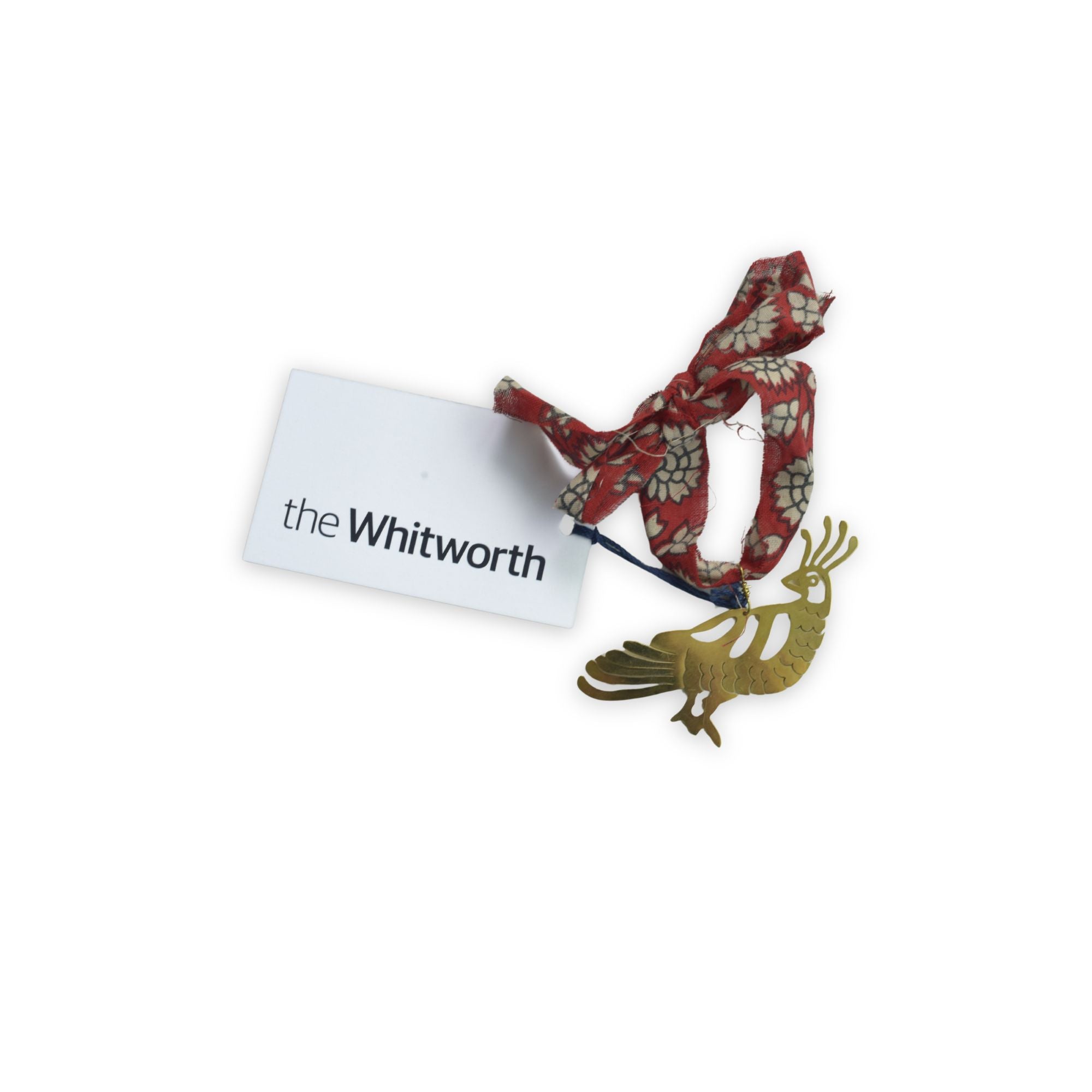 A red and white floral ribbon loop attached to a gold-toned metal bird decoration, with a white tag labelled 'the Whitworth'.