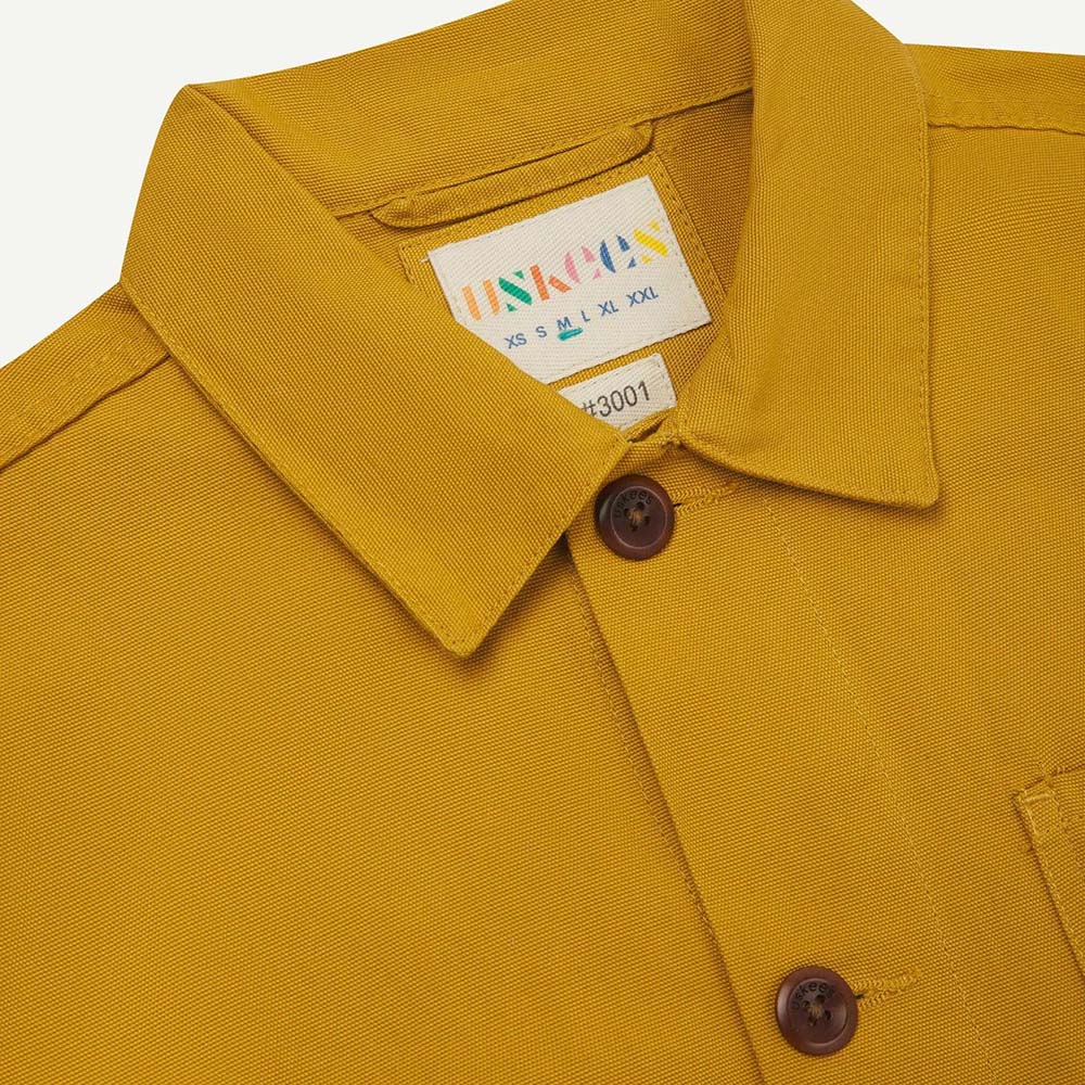 Close-up of a mustard yellow shirt with a brand label on a white background