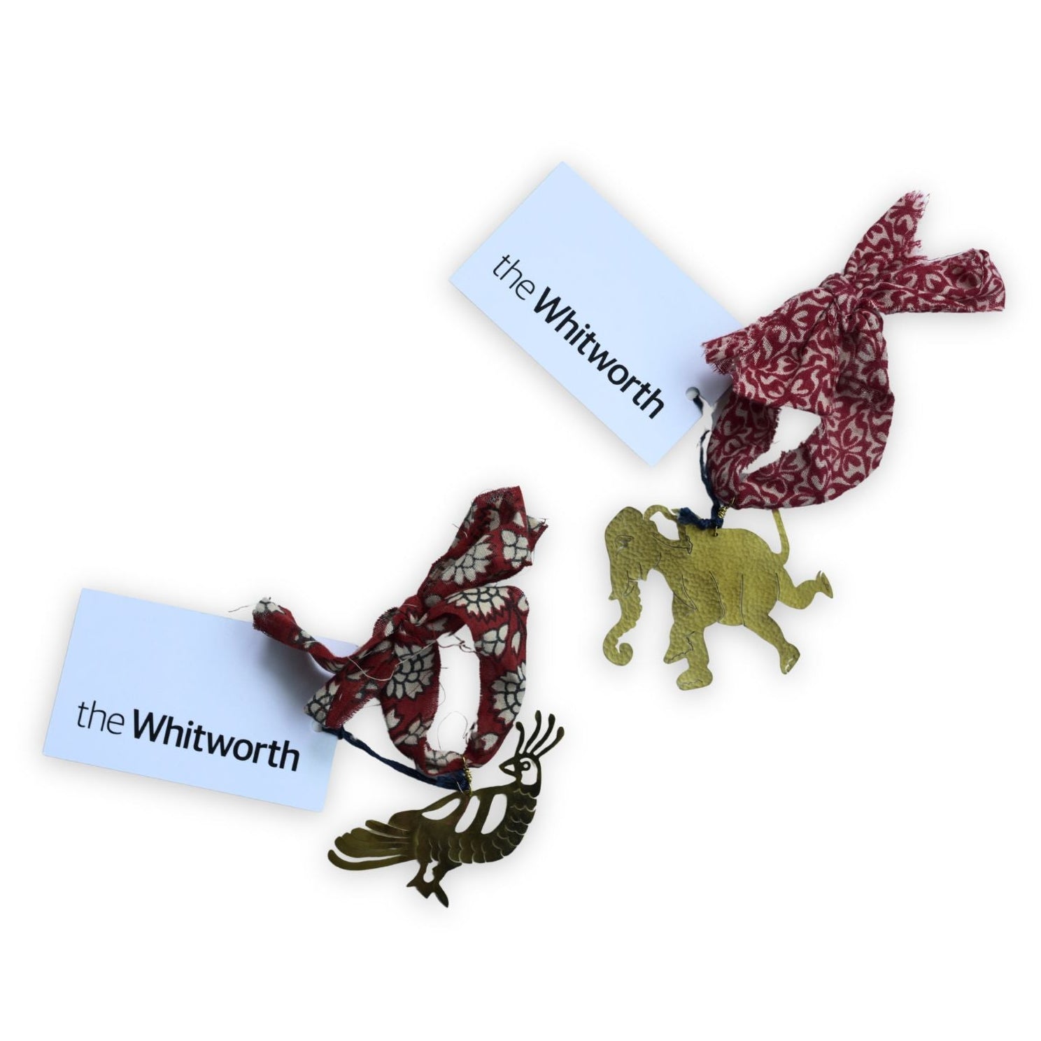Two brass decorations on a white background. The one to the bottom left is a peacock and the one to the top right is an elephant. Both decorations have a colourful fabric ribbon attached and a white swing tag printed with 'the Whitworth' in black.