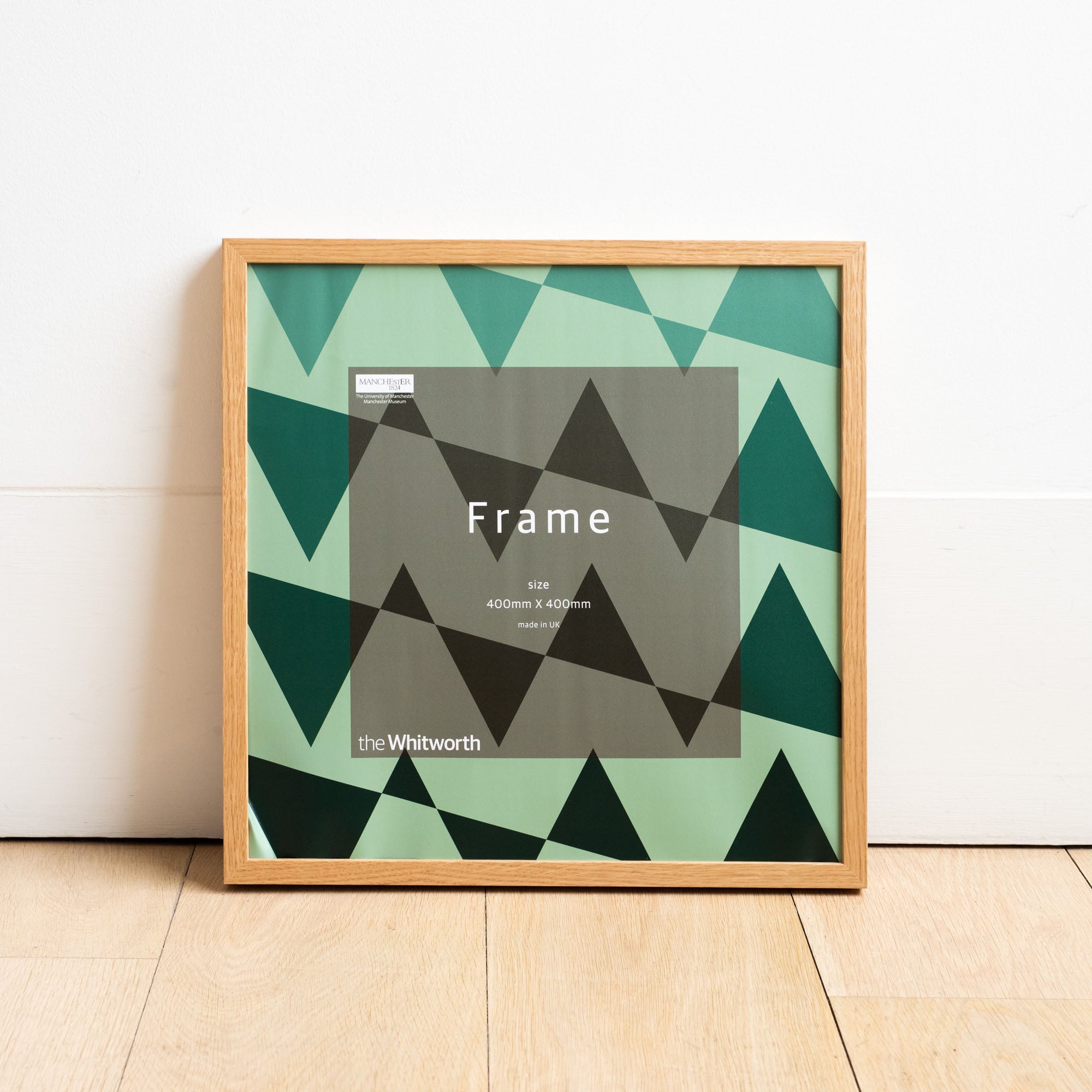Natural ash square frame. Whitworth branded backing paper inside which is a green triangular pattern.