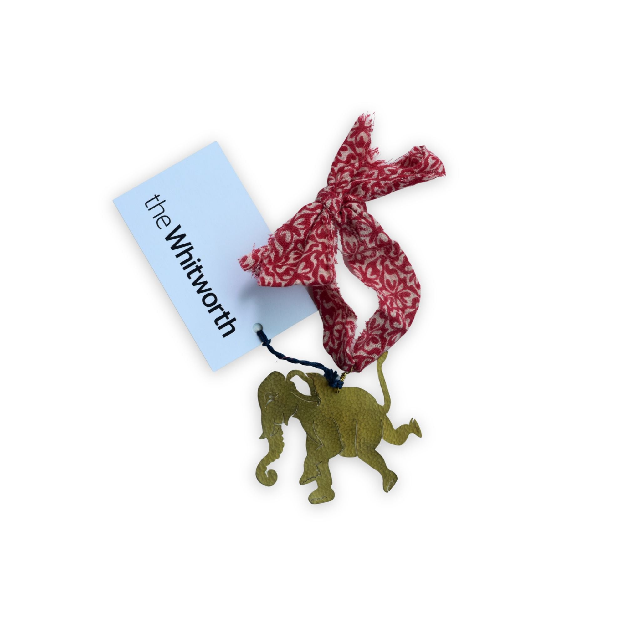 A small elephant-shaped brass decoration with a red and white patterned fabric ribbon attached to a swing tag printed with 'the Whitworth'.