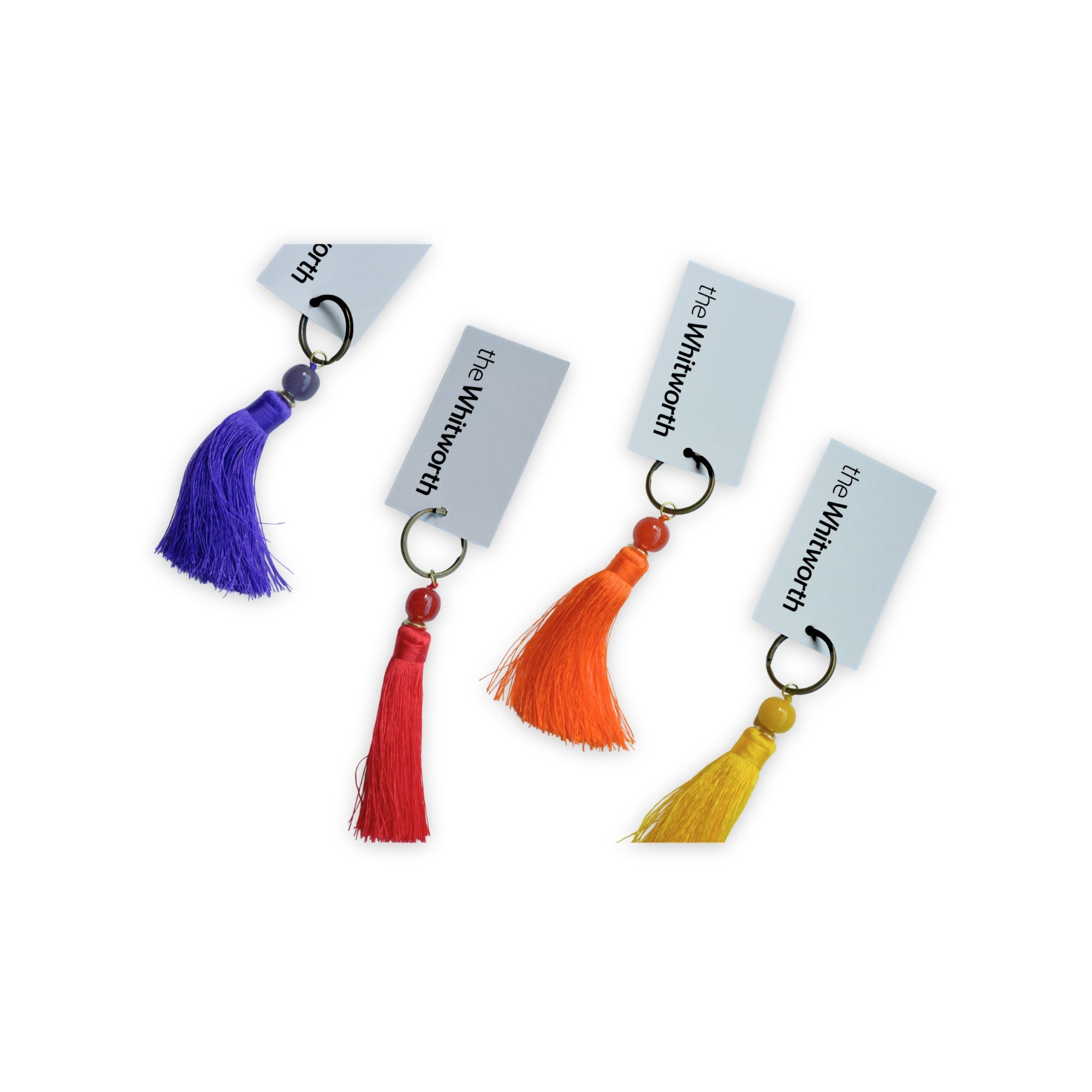 Four colorful tassels with beads and metal key rings, each attached to a swing tag printed with 'the Whitworth', shown on a plain white background.