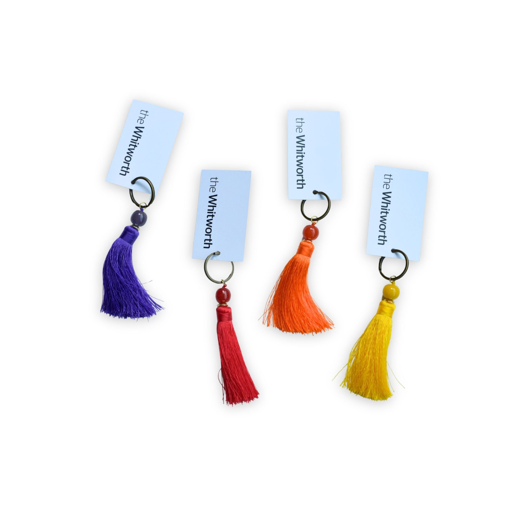 Four tassel keychains with white swing tags reading 'the Whithorn' arranged on a white background. The tassels are purple, red, orange, and yellow, each attached to a metal key ring.