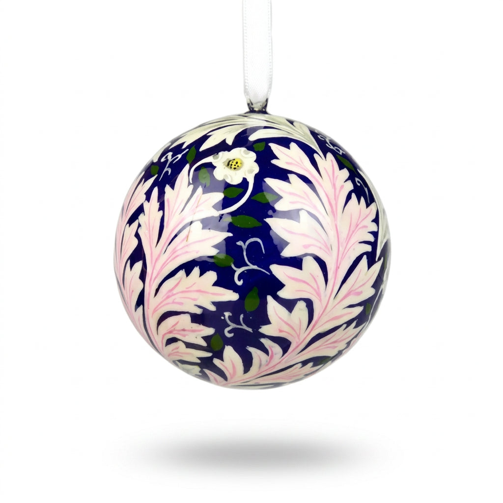 A spherical Christmas bauble featuring a William Morris-style floral pattern with white and light pink leaves on a dark navy blue background, suspended by a white string.