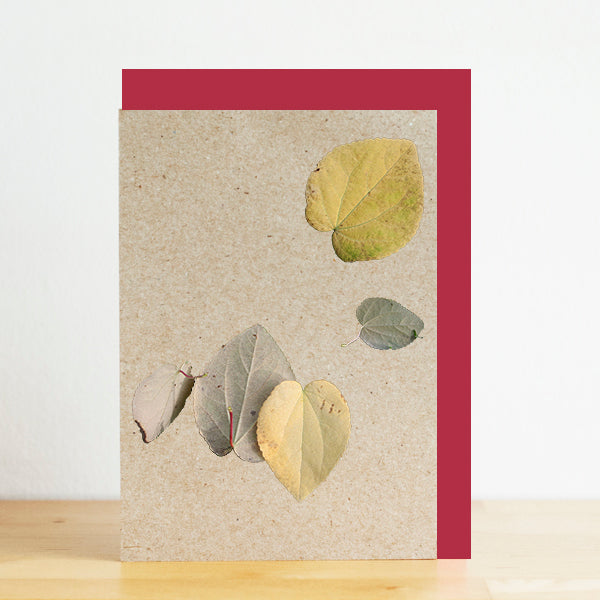 Card with pressed leaves on a textured beige background with a red border