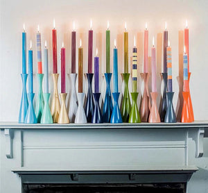 Colourful candles in various holders on a white surface
