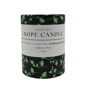 A black cylindrical candle container with a white label featuring green vines sits on a white background.