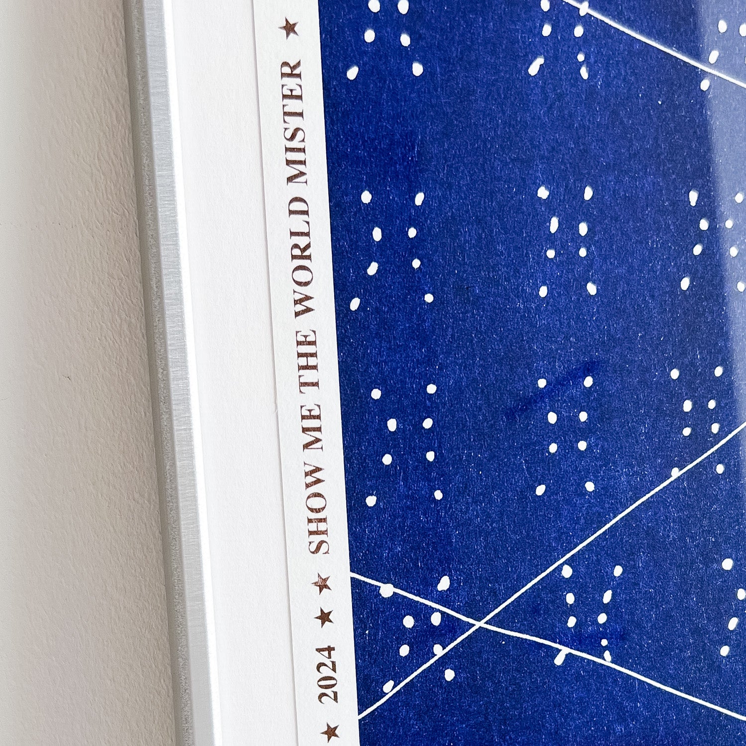Close up of an artwork by Ayo Akingbade in a silver frame. You can see the border edge of the print with the words 'SHOW ME THE WORLD MISTER'.