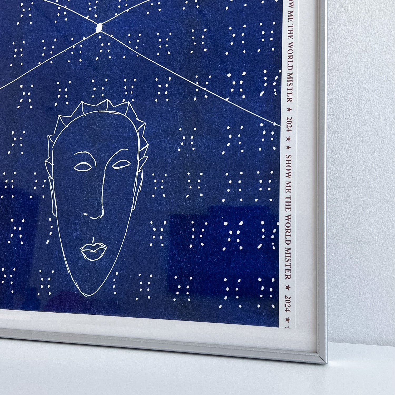 Close up of an artwork by Ayo Akingbade in a silver frame. You can see the border edge of the print with the words 'SHOW ME THE WORLD MISTER'.