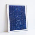 Artwork by Ayo Akinbade in silver frame resting against a white wall. Blue and white repeat dot pattern with a head of a person in white outline at the bottom.