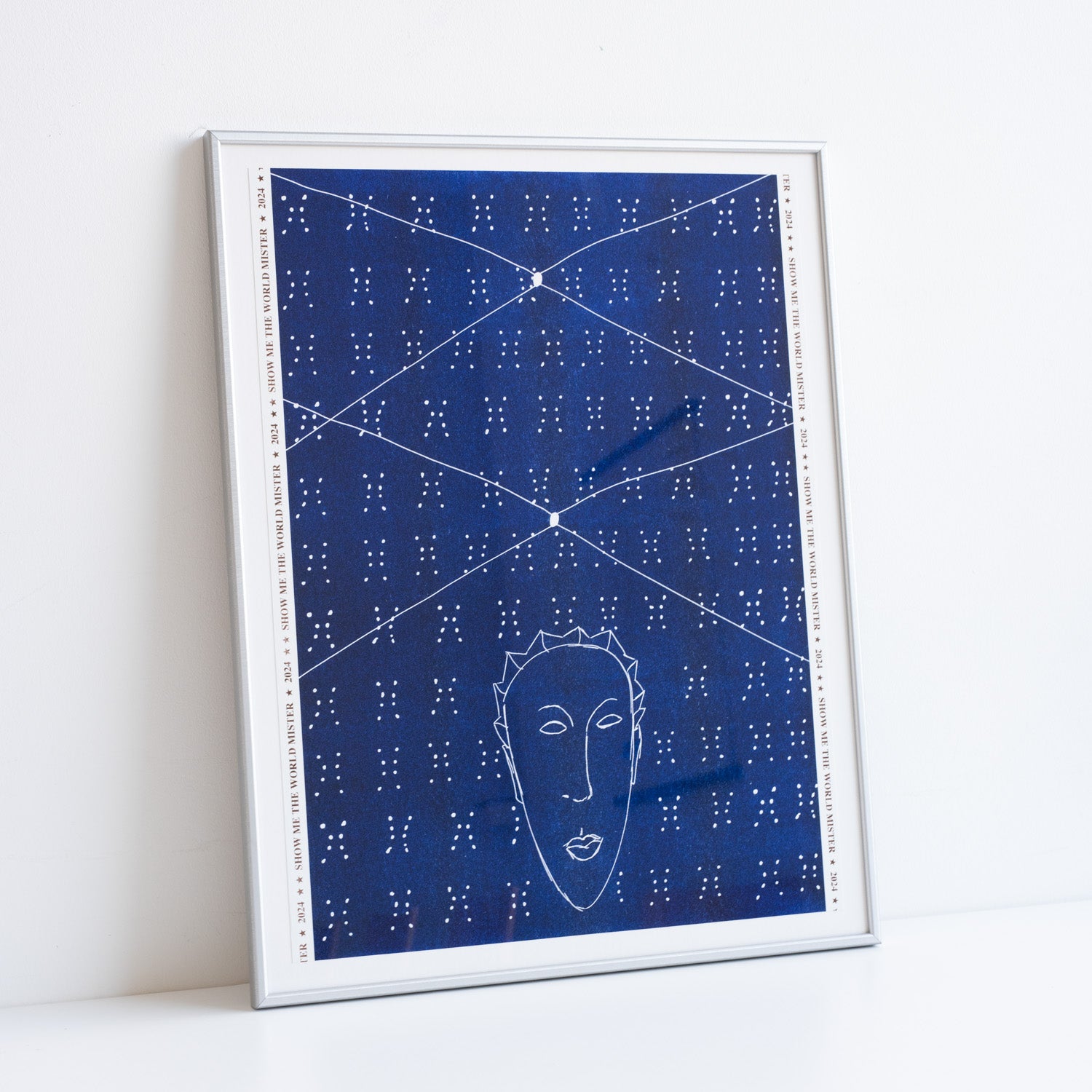 Artwork by Ayo Akinbade in silver frame resting against a white wall. Blue and white repeat dot pattern with a head of a person in white outline at the bottom.