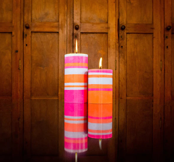 Two pink, orange and white striped candles in front of a brown cupboard