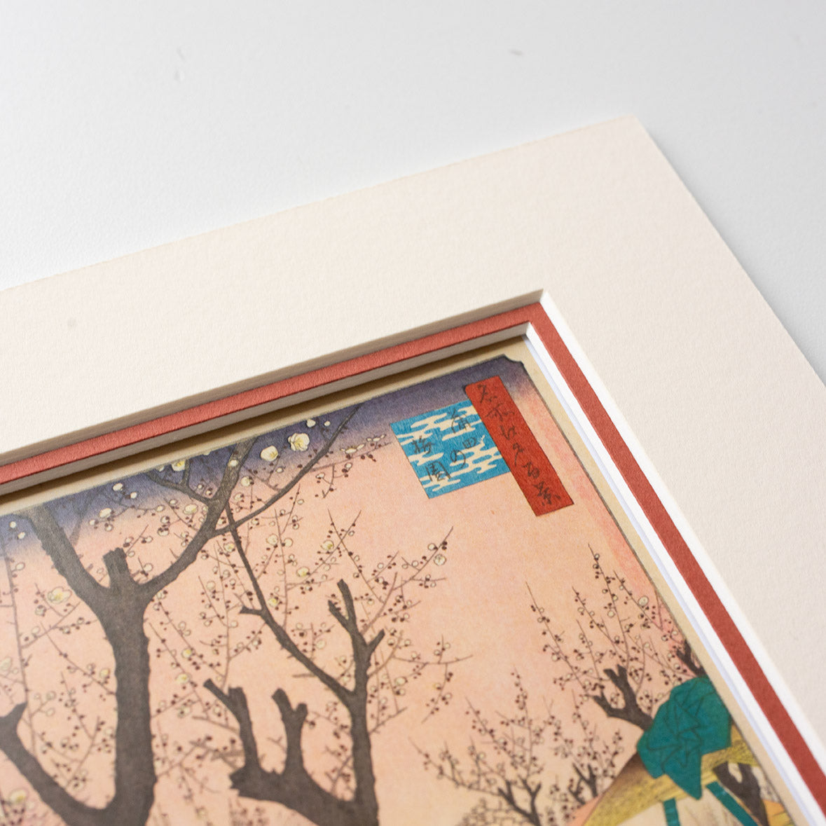Detail of corner of mounted artwork of a cherry blossom tree scene on a light grey background