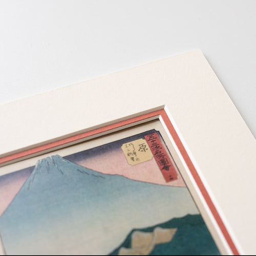 Detail of corner of mounted artwork of a mountain landscape with a red mount on a light grey background