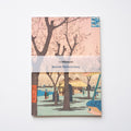Notebook cover with cherry blossom trees and a scene of people by a river, featuring 'the Whitworth' branding.