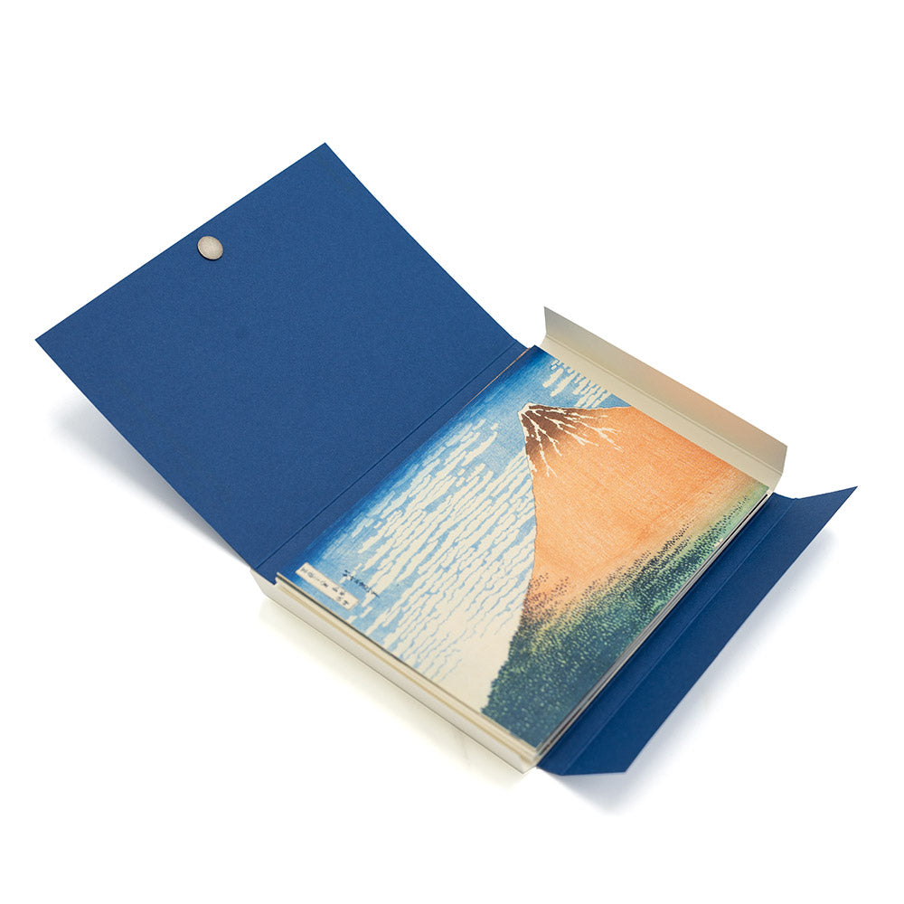 Open postcard set with a blue cover and a postcard of a mountain illustration, presented on a white background