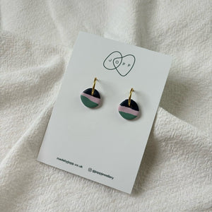 A pair of handmade hoop earrings by JOPP Jewellery. Each earring features a circular disc with layers of pink, green, and black polymer clay, hanging from a gold-toned hoop.