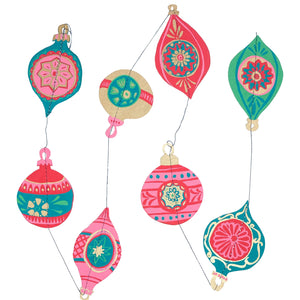 Festive paper bauble hanging decoration. The baubles are in various shapes and sizes, with intricate patterns and designs in shades of pink, green, gold, and red. They are connected by a thin string.