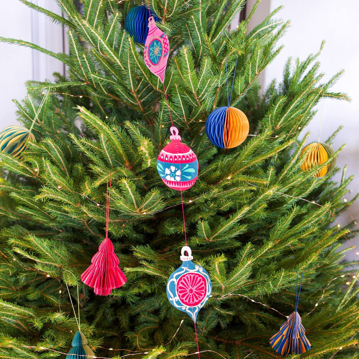 Christmas tree decorated with a variety of paper ornaments. The ornaments are in different shapes and sizes, with intricate patterns and designs in vibrant colours. 