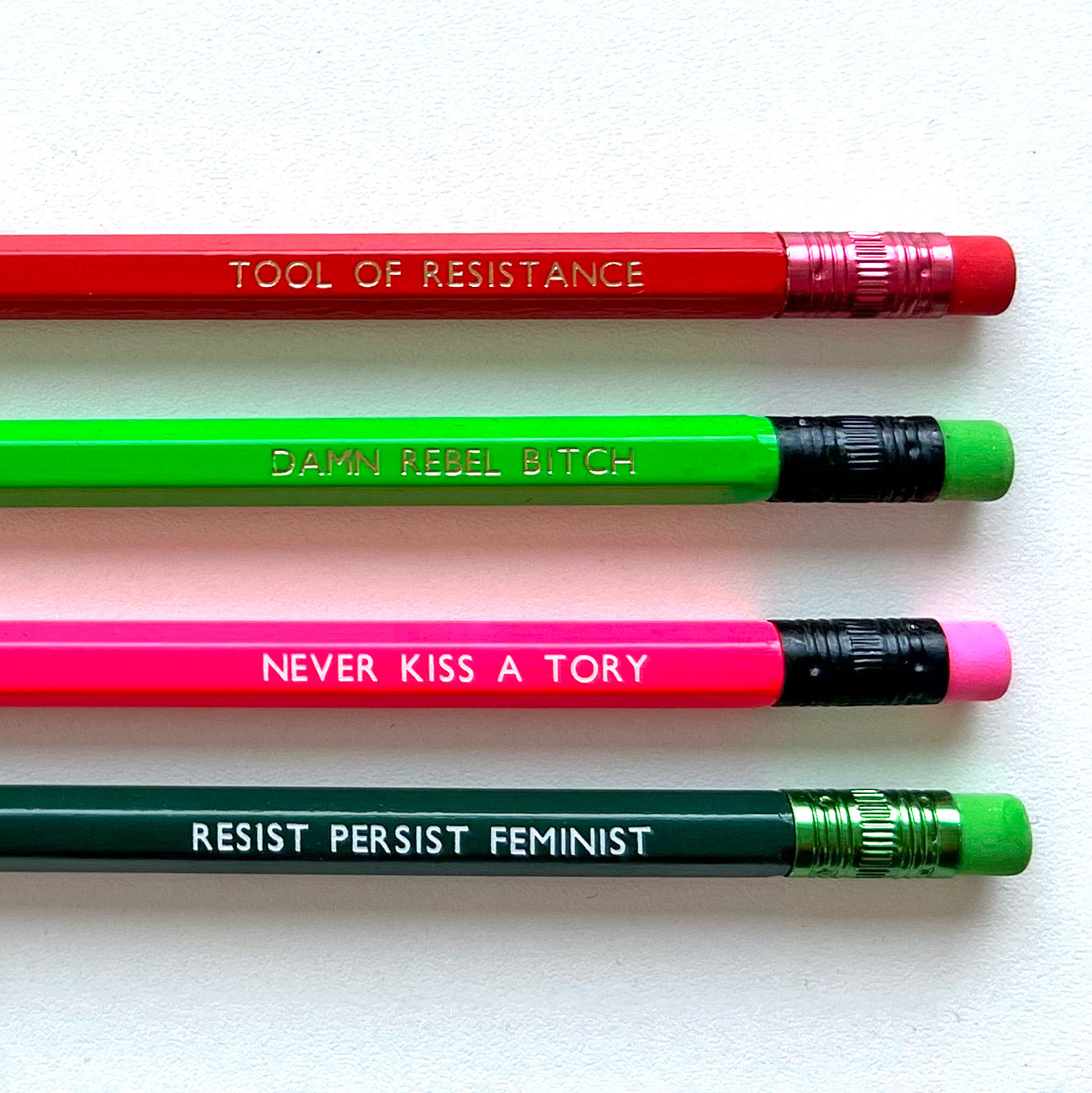 Four colourful pencils with feminist slogans are arranged diagonally on a light background.