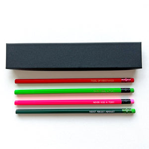 Four colourful pencils with feminist slogans are arranged diagonally on a light background.