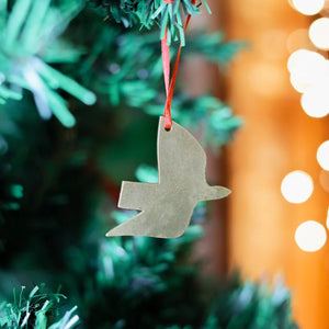 Close up photograph of a brass decoration in the shape of a dove, on a Christmas tree with some lights in the background.