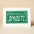 A green and white Christmas card featuring the phrase "BRUSSELS SPROUTS" in a playful, hand-lettered style. The card stars and decorative elements framing the text.