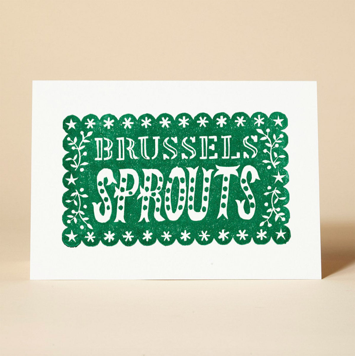 A green and white Christmas card featuring the phrase "BRUSSELS SPROUTS" in a playful, hand-lettered style. The card stars and decorative elements framing the text.