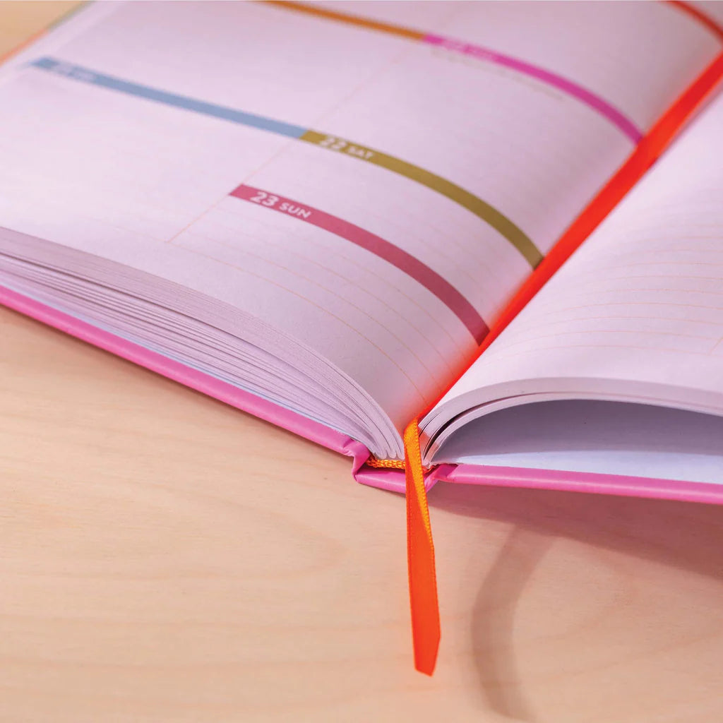 A close-up of an open pink diary with a bright orange ribbon bookmark. The pages are blank and ready for writing.