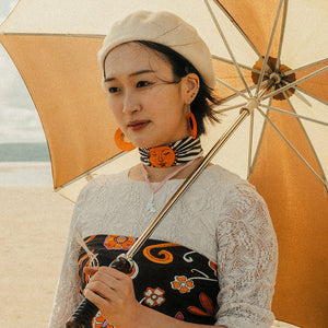 Person holding an orange umbrella on a beach, wearing the scarf