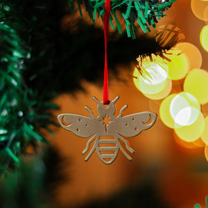 Close up photograph of a brass decoration in the shape of a bee, on a Christmas tree with some lights in the background.