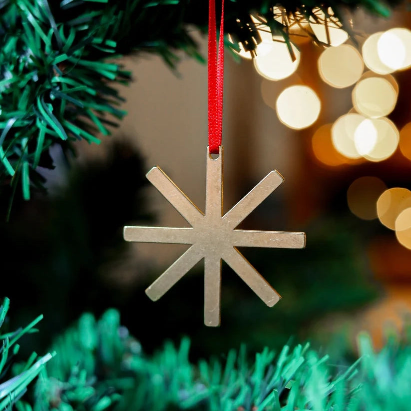 Close up photograph of a brass decoration in the shape of a star, on a Christmas tree with some lights in the background.