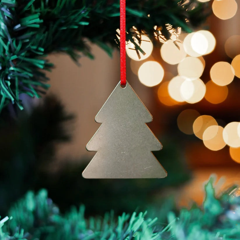 Close up photograph of a brass decoration in the shape of a tree, on a Christmas tree with some lights in the background.
