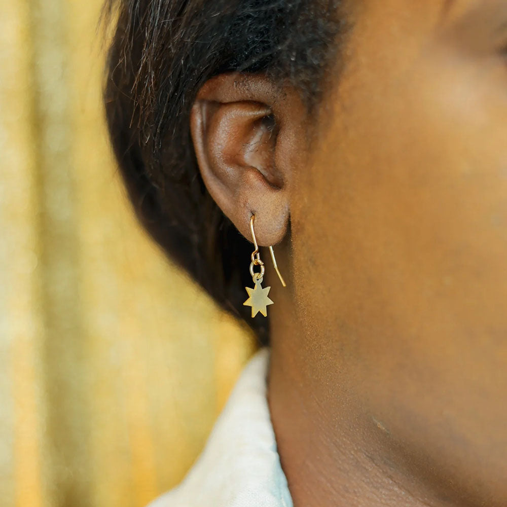 A close up of a person wearing the gold earrings