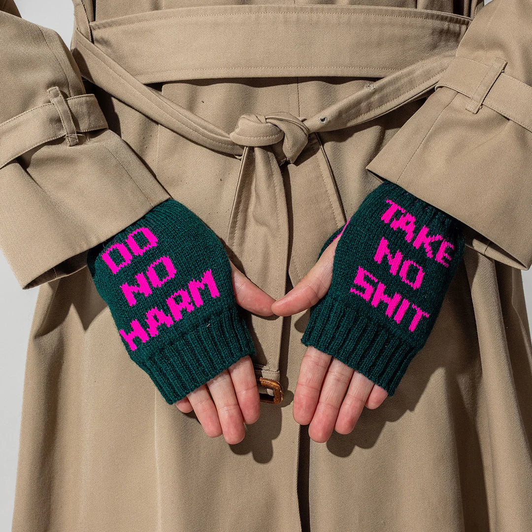 Person wearing a beige trench coat with green fingerless gloves displaying pink text.