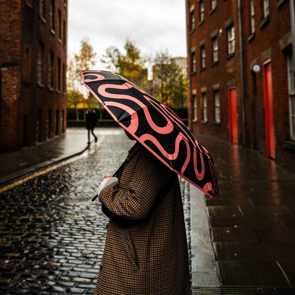 Person holding a black umbrella with red patterns on a cobblestone street.