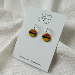 A pair of handmade polymer clay hoop earrings by JOPP Jewellery. The earrings feature circular orange and yellow discs with black stripes, hanging from silver-toned hoops.