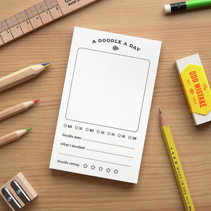 Notebook with 'A Doodle a Day' template on a wooden surface with stationery items.