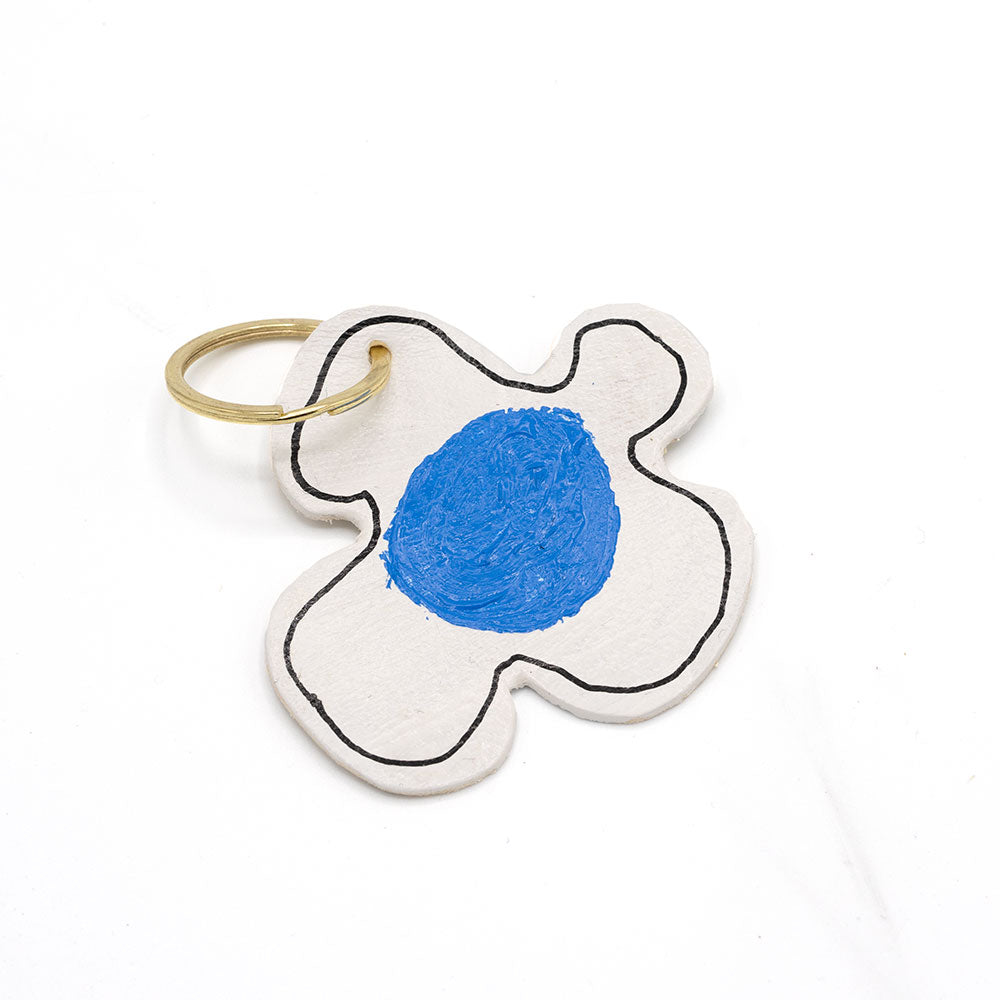 Keyring in the shape of a flower with white petals and a blue centre. Photographed in front of a white background.