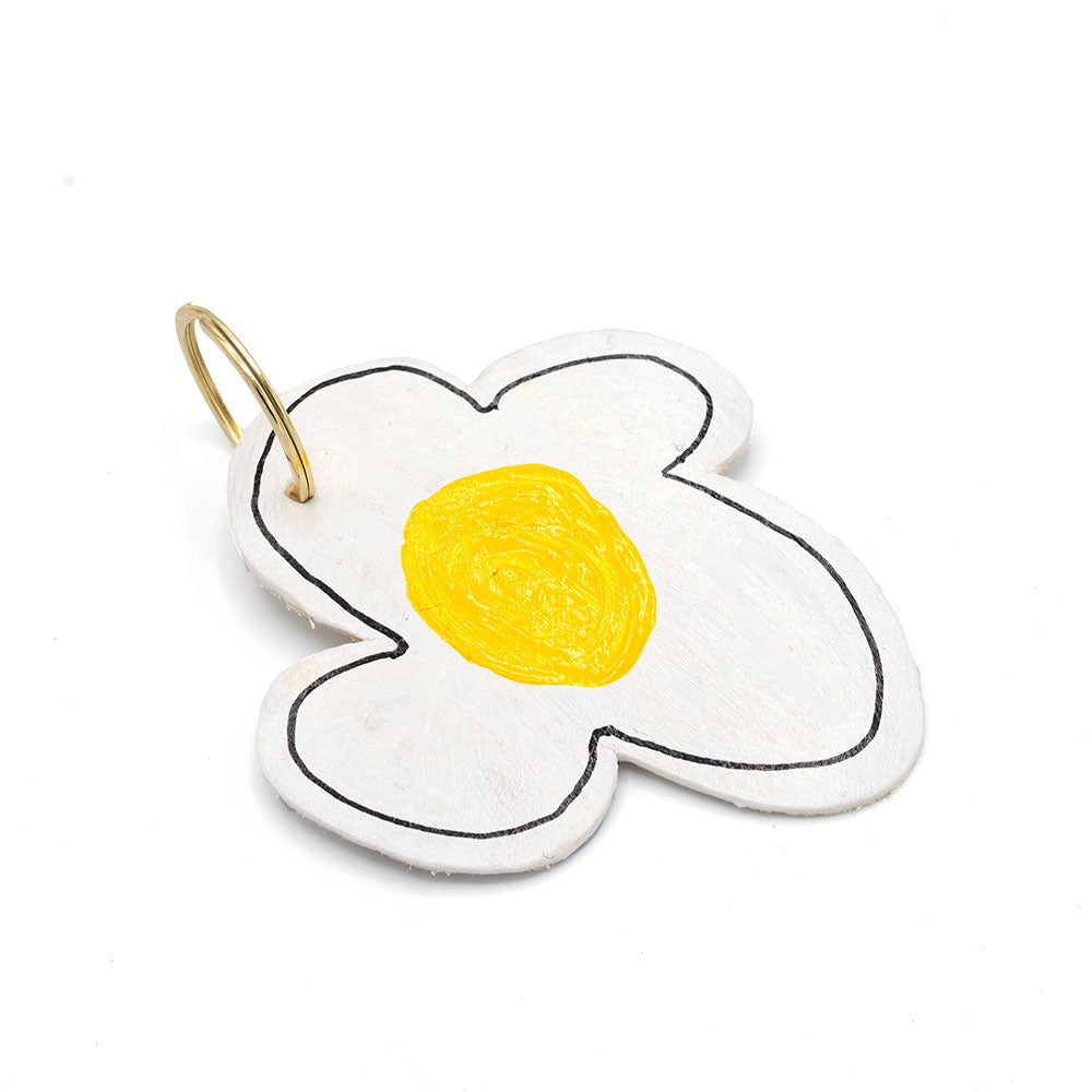 Keyring in the shape of a flower with white petals and a yellow centre. Photographed in front of a white background.