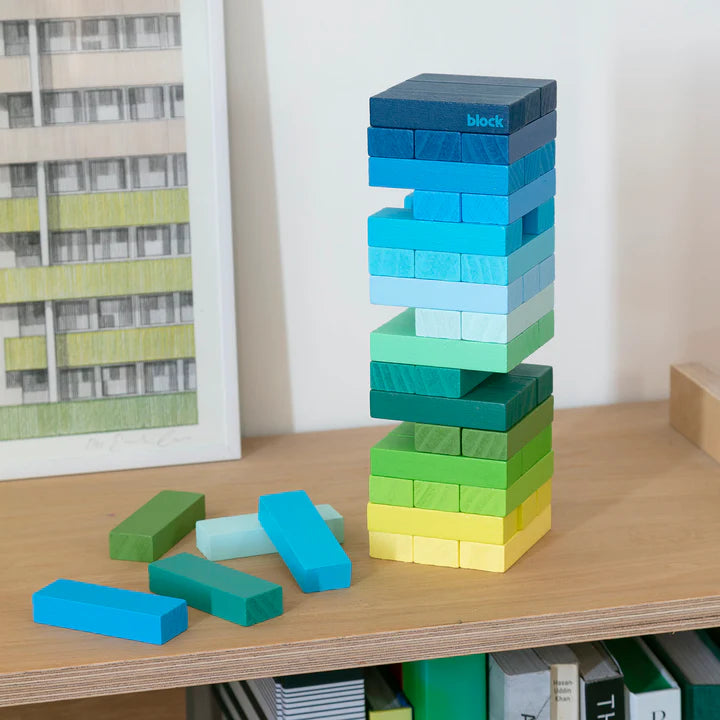 A tower of colourful wooden blocks stacked on top of each other. The blocks are in shades of blue, green, and yellow. There are a few blocks on the side of the tower. The word "block" is written on the top block.