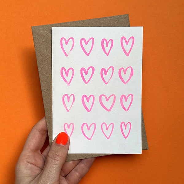 A person holding up a card with love hearts against an orange background.