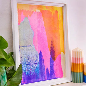 Purple, orange and pink abstract risograph print in white frame leaning against a wall.