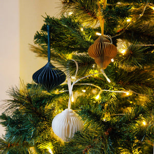 Three paper decorations in white, yellow, and teal, hanging from strings on a Christmas tree.