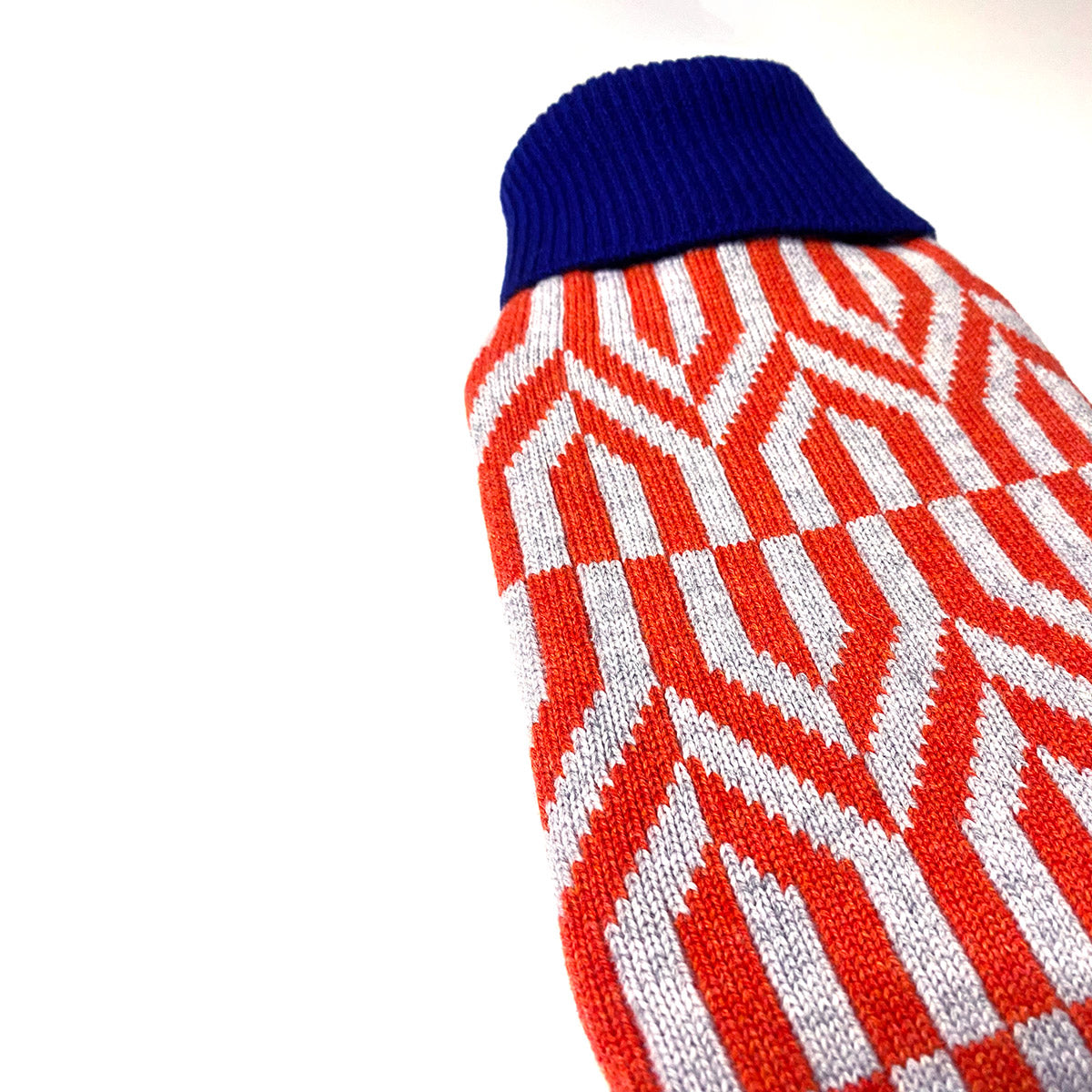 Hot water bottle with hand knitted cover in a geometric red, grey and blue pattern.